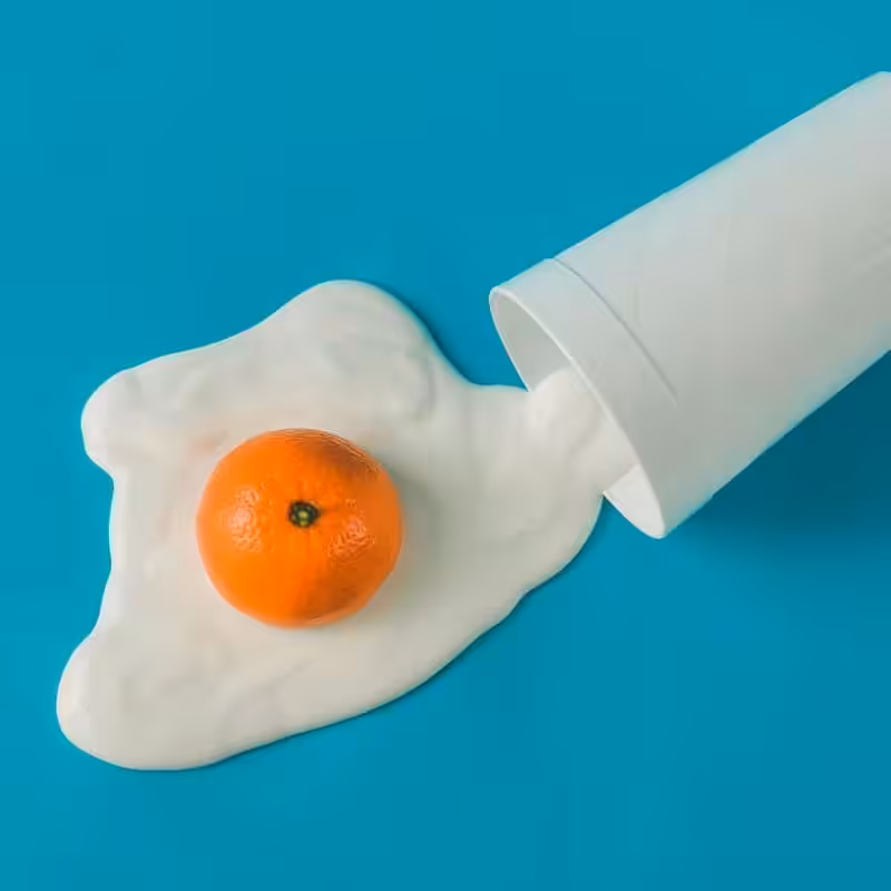 Fresh orange trapped in spilled white yogurt with a white cup on vibrant blue background.