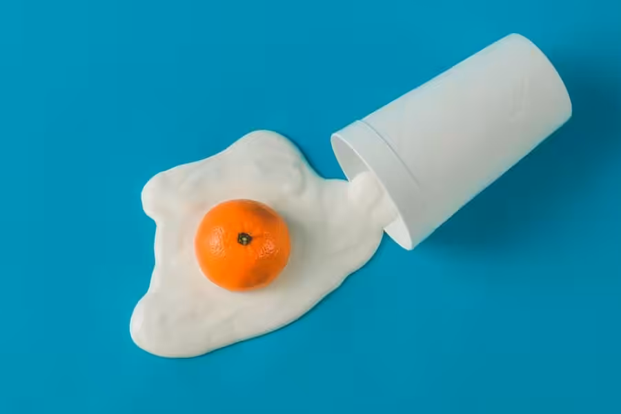 Fresh orange trapped in spilled white yogurt with a white cup on vibrant blue background.