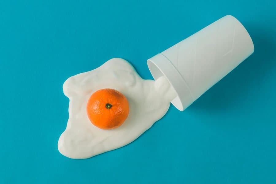 Fresh orange trapped in spilled white yogurt with a white cup on vibrant blue background.